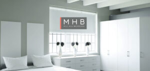 The MHB logo overlaid on a view of a bedroom with fitted furniture